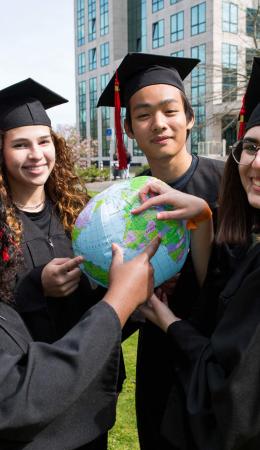 Students with a graduation hat pointing at the Netherlands on a globe