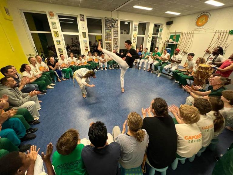 People sitting in a circle look at two people practising capoeira in the center