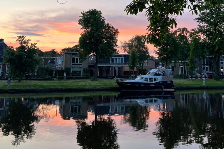 Body of water with a boat in the distance, in front of houses. Sunset in the background